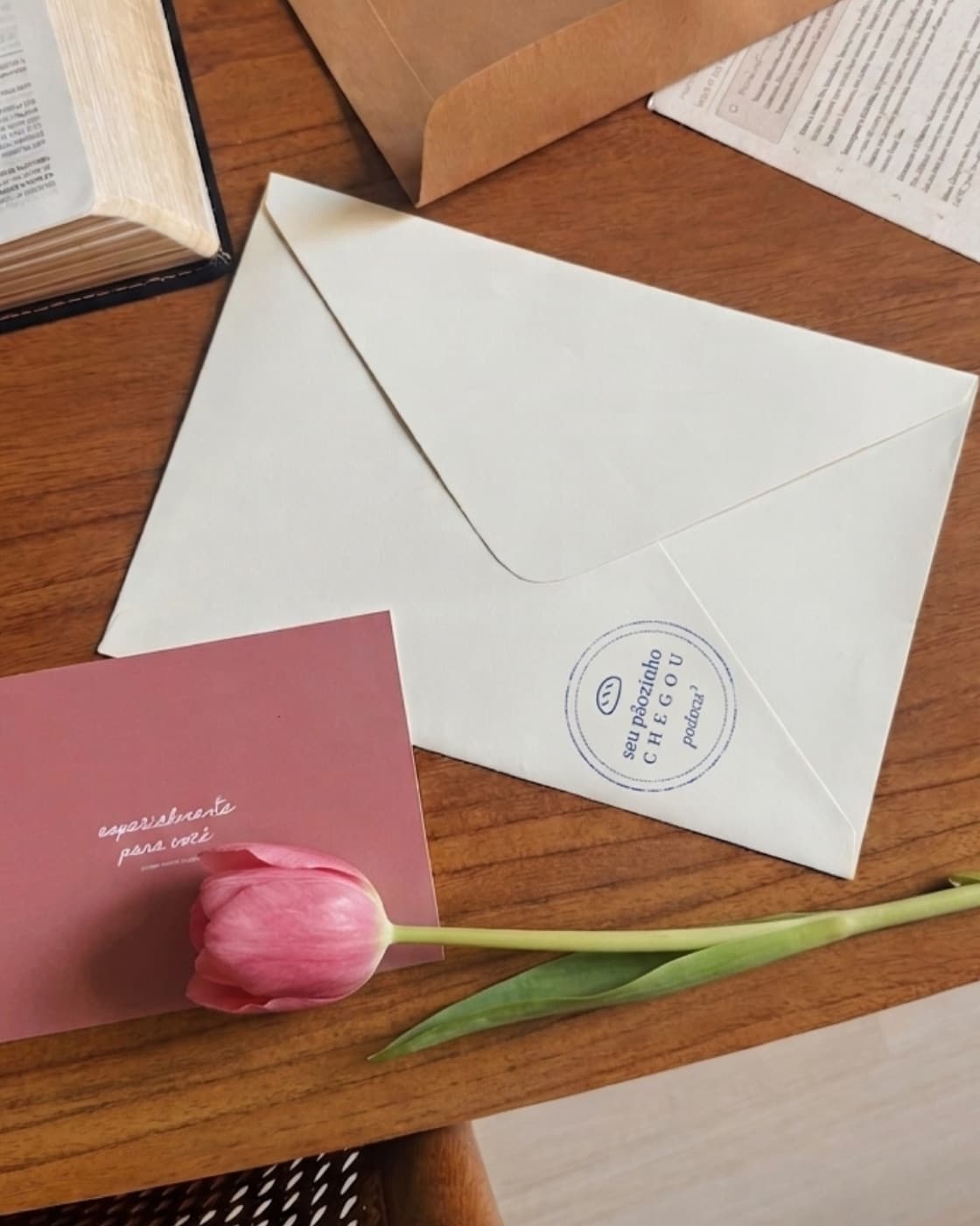 Envelope da Padoca³ com carimbo, cartão e uma tulipa sobre a mesa
